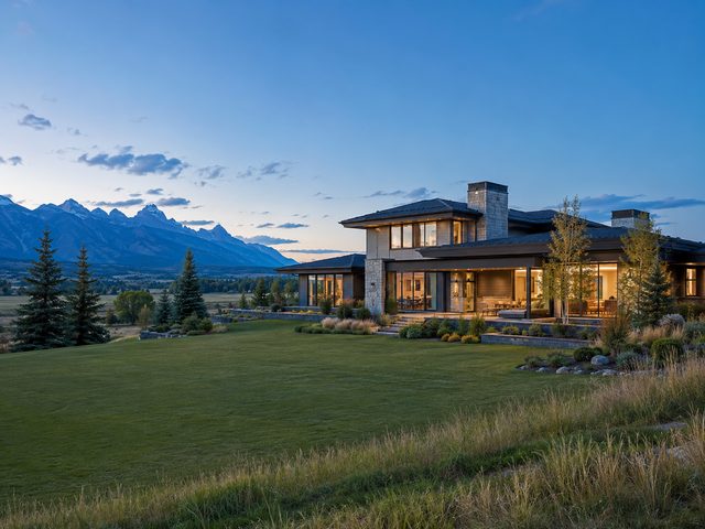 An estate home on open acreage at dusk with mountains along the western horizon.